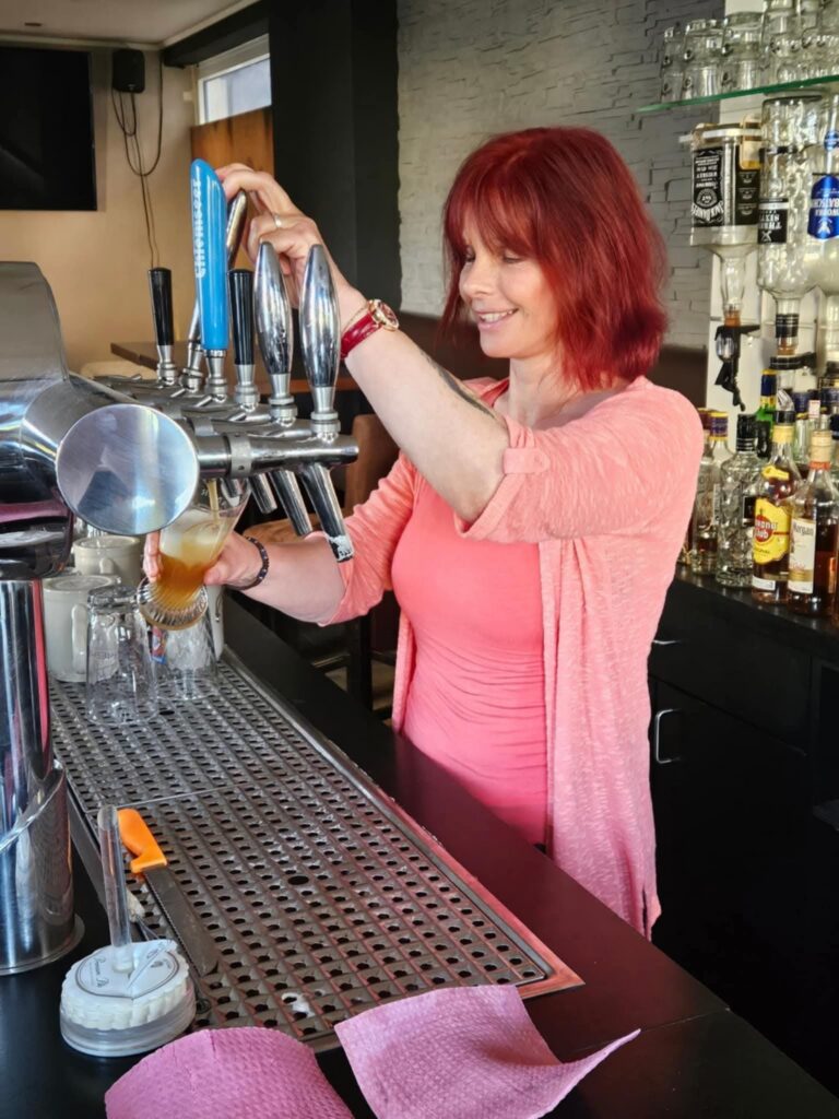 Cerstin steht hinter dem Tresen der Fußballkneipe "Abseits" in Schriesheim und zapft zum ersten Mal selbst ein Weißbier frisch vom Fass. Die Szene wirkt herzlich, lebendig und vermittelt die besondere Atmosphäre des Abends.